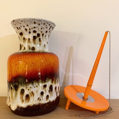 Västttysk retrovas i orange-brunt s k lavamönster, till höger om vasen en orange kulspetspenna i ställ (Ballograf Deskset).